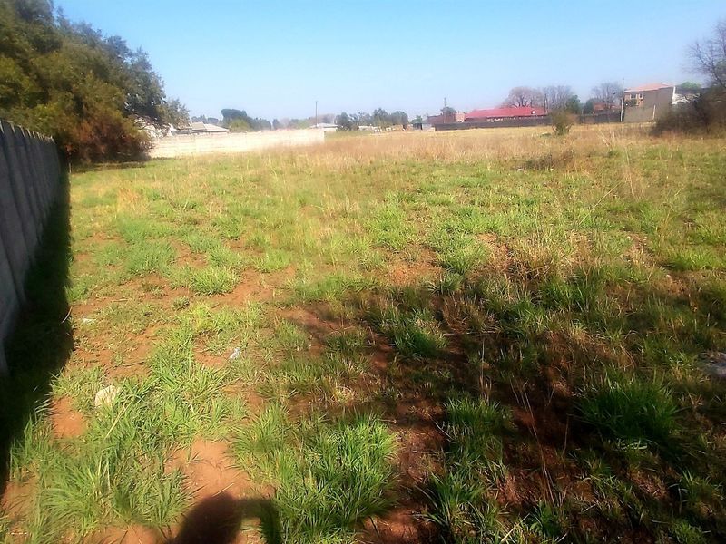 A vacant residential plot featuring a precast concrete boundary wall and natural grass coverage.