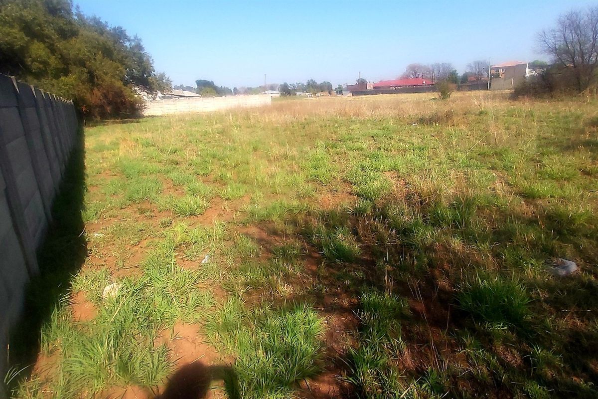 A vacant residential plot featuring a precast concrete boundary wall and natural grass coverage.