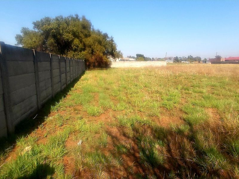A vacant residential plot featuring a long precast concrete boundary wall and natural grass coverage.