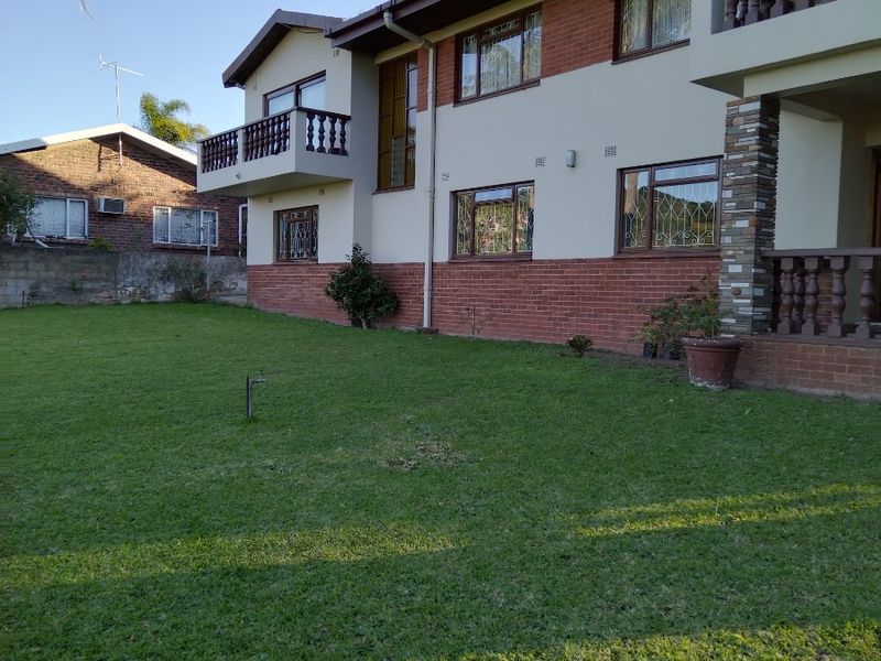 Rear view of a multi-story residential property featuring a brick and plaster facade, balconies, and a well-maintained lawn area.