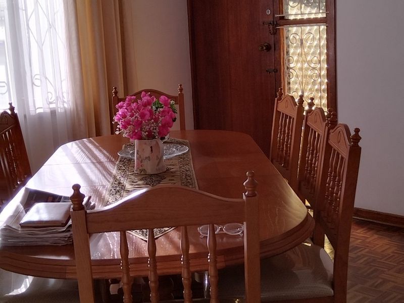 A dining room featuring traditional parquet flooring, a solid timber door with a security gate, and a window with a decorative curtain pelmet.