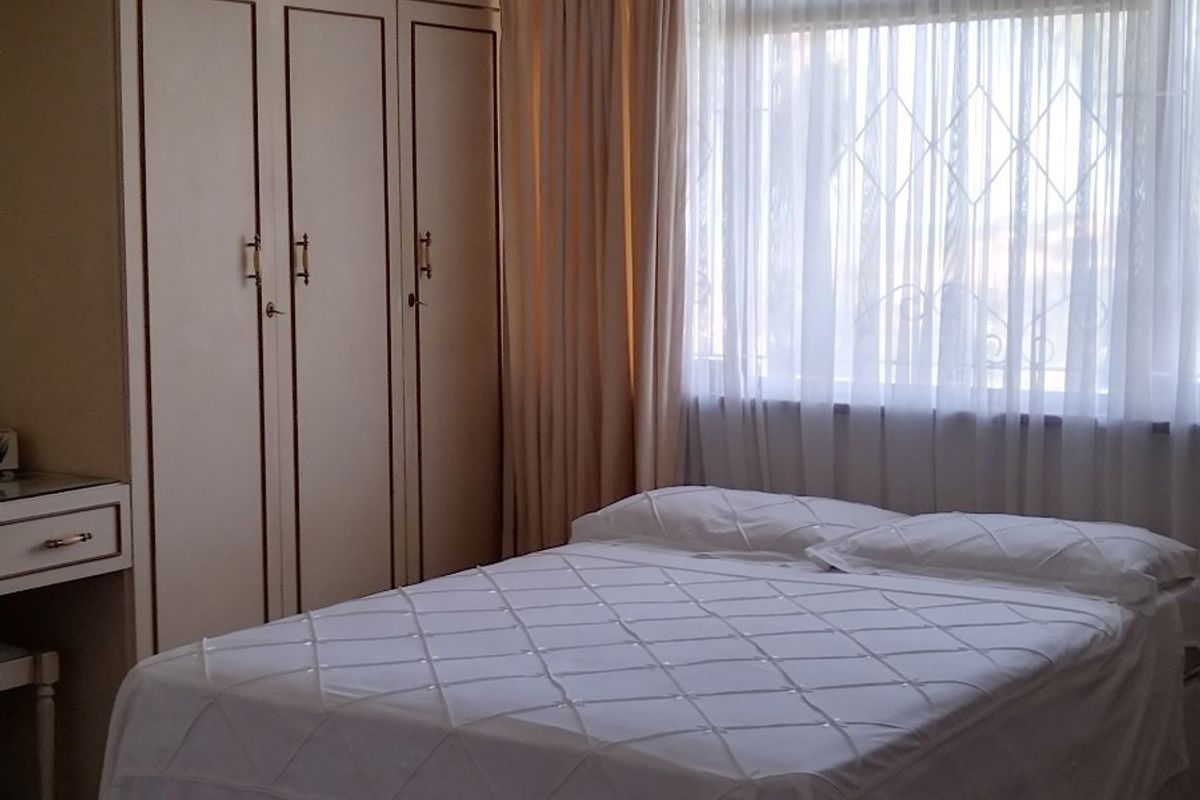 A bedroom featuring built-in cupboards with an integrated vanity, parquet flooring, and security bars on the window.