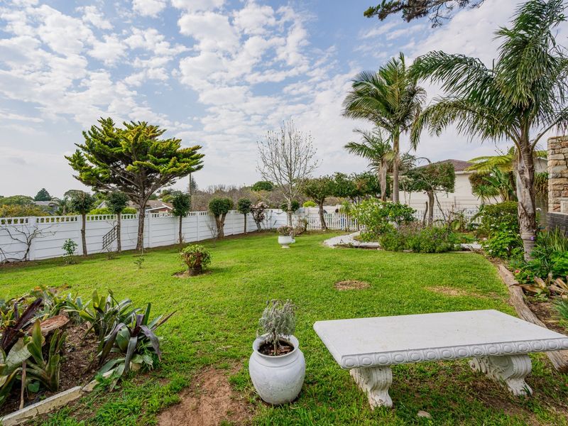 A well-maintained rear garden featuring a lush lawn, established palm trees, and secure white perimeter fencing.