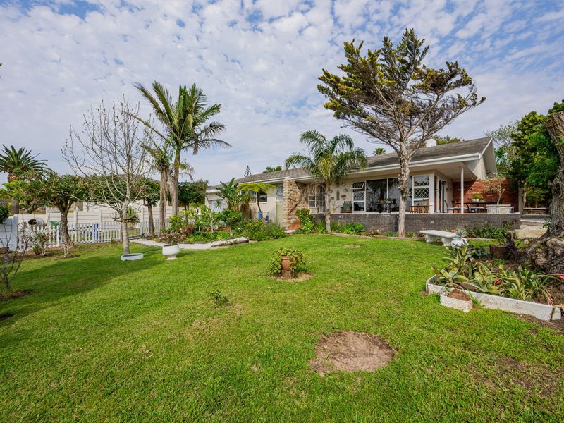A spacious rear garden featuring a well-maintained lawn, mature trees, and a covered patio area attached to the main house structure.