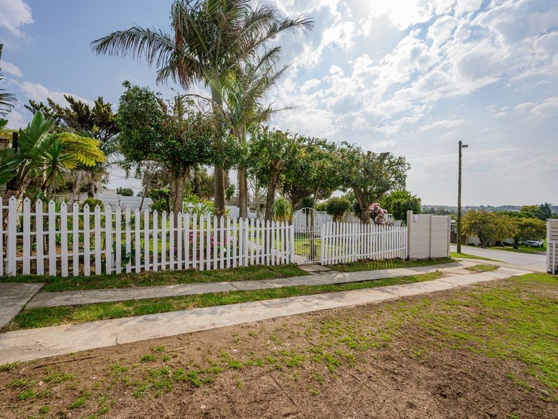 Front view of the property featuring a white picket fence, pedestrian gate, and established garden with mature trees.
