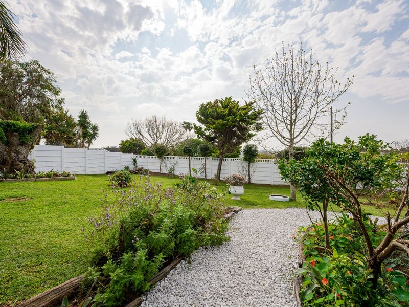 A well-maintained rear garden featuring a gravel pathway, established trees, and secure white perimeter fencing.