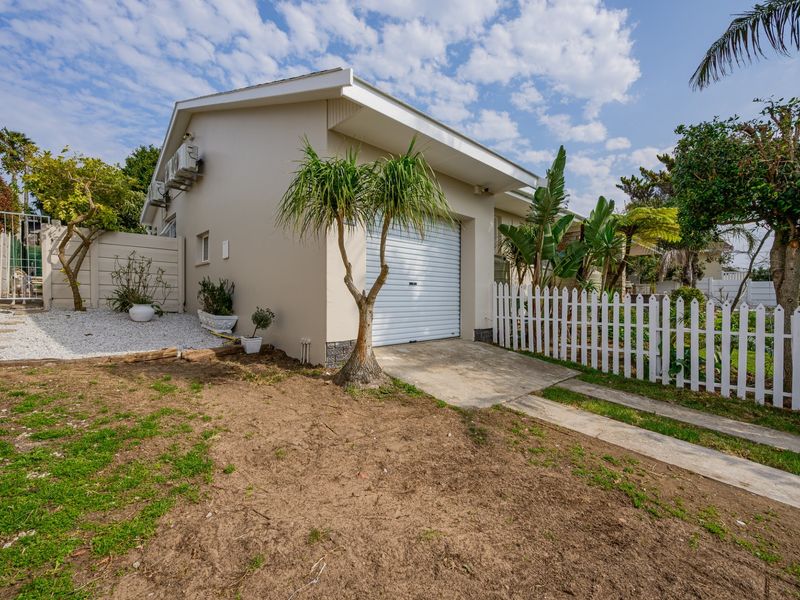 Front exterior view of the property featuring a single garage, concrete driveway, and white picket fencing with established garden elements.
