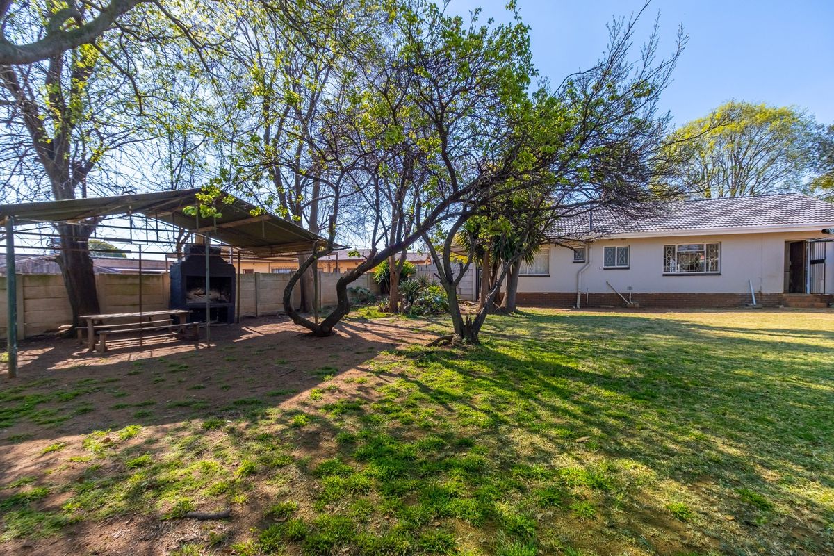Spacious rear garden featuring a large lawn, mature trees, and a covered outdoor entertainment area with a built-in braai.
