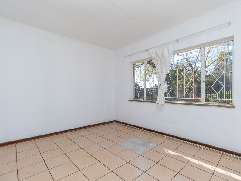An empty bedroom featuring tiled flooring, coved ceilings, and a window fitted with security burglar bars.