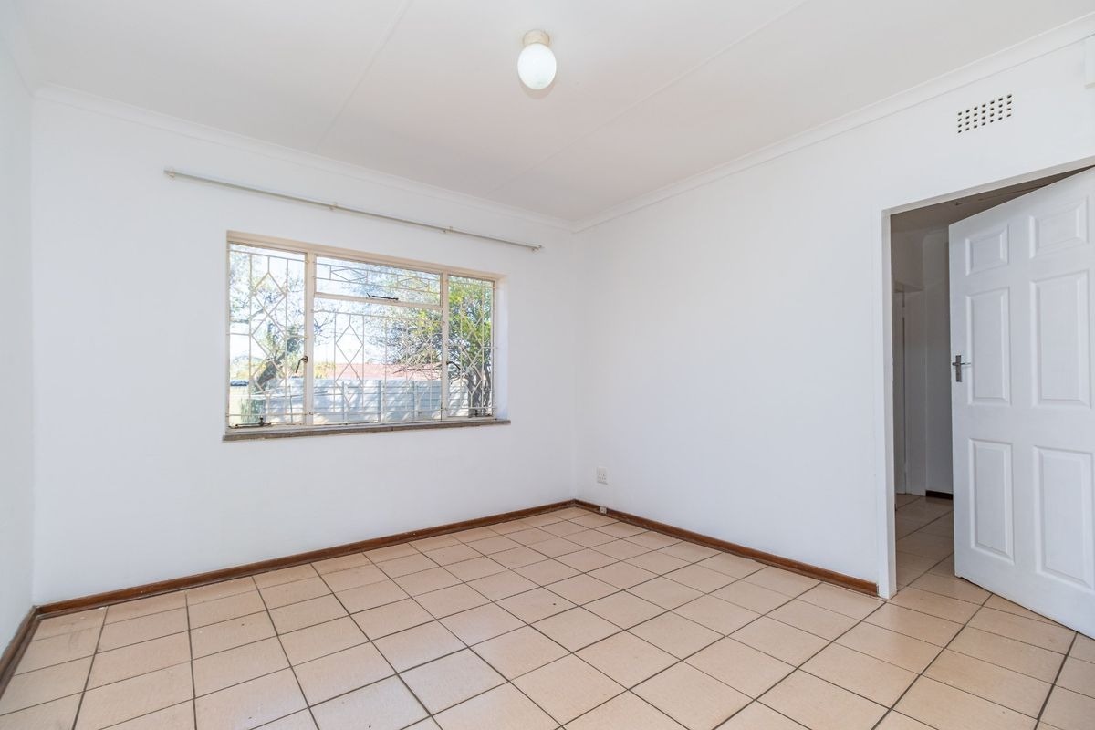 A vacant bedroom featuring neutral tiled flooring, white walls, and a window fitted with security bars.
