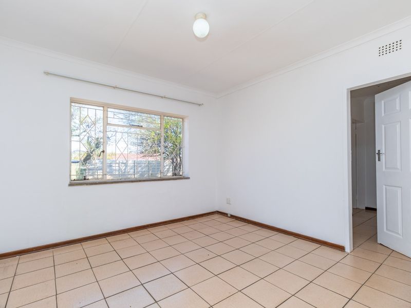 A vacant bedroom featuring neutral tiled flooring, white walls, and a window fitted with security bars.