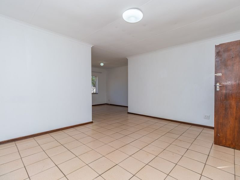 An empty, open-plan living area featuring neutral tiled flooring, white walls, and a wooden door, offering a blank canvas for interior design.