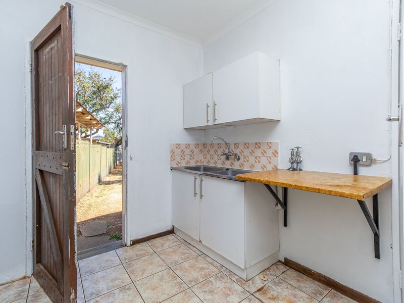 A functional scullery or utility area featuring a stainless steel sink, wall-mounted cabinetry, and direct access to the rear exterior.