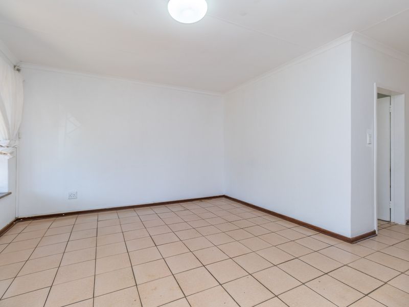 A bright, empty living area featuring neutral white walls, tiled flooring, and security bars on the window, offering a blank canvas for interior design.