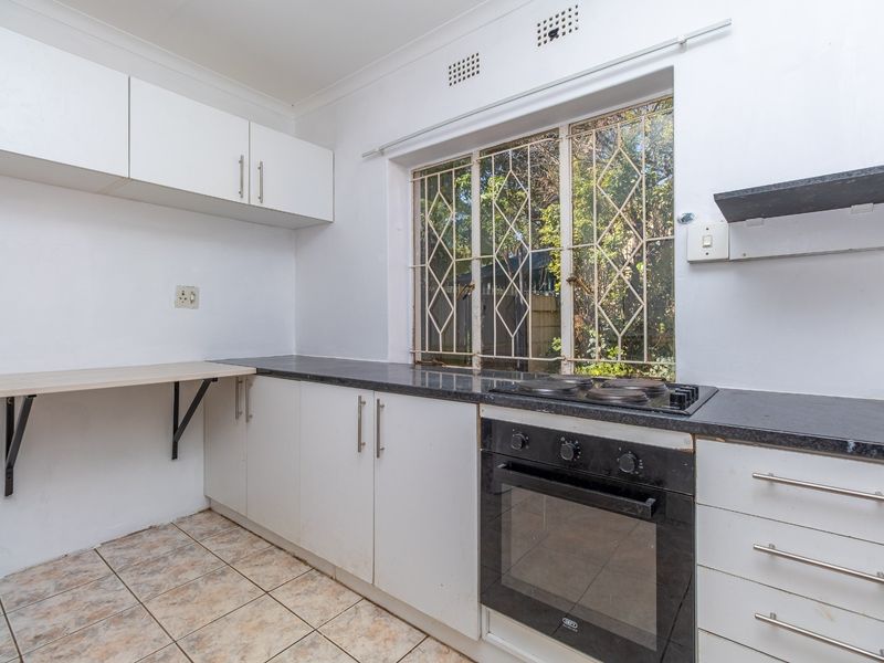 A functional kitchen featuring white cabinetry, dark countertops, a built-in oven and hob, and tiled flooring with a window overlooking the garden.