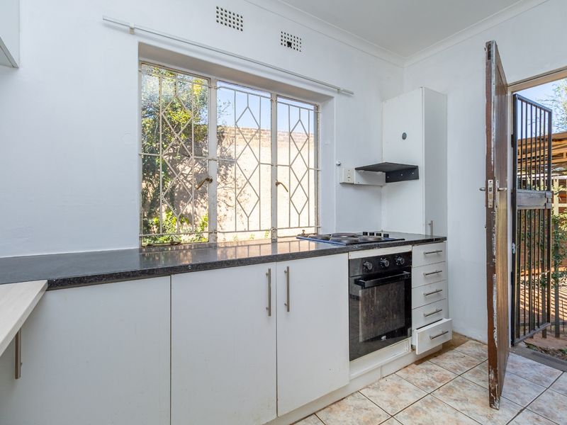 A functional kitchen featuring built-in cabinetry, stone countertops, a built-in oven with gas hob, and direct access to the exterior via a security gate.