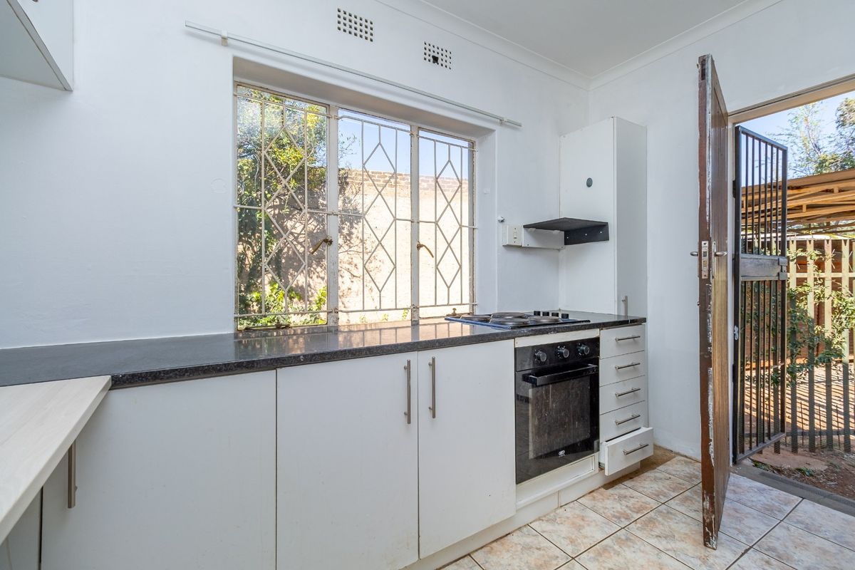 A functional kitchen featuring built-in cabinetry, stone countertops, a built-in oven with gas hob, and direct access to the exterior via a security gate.