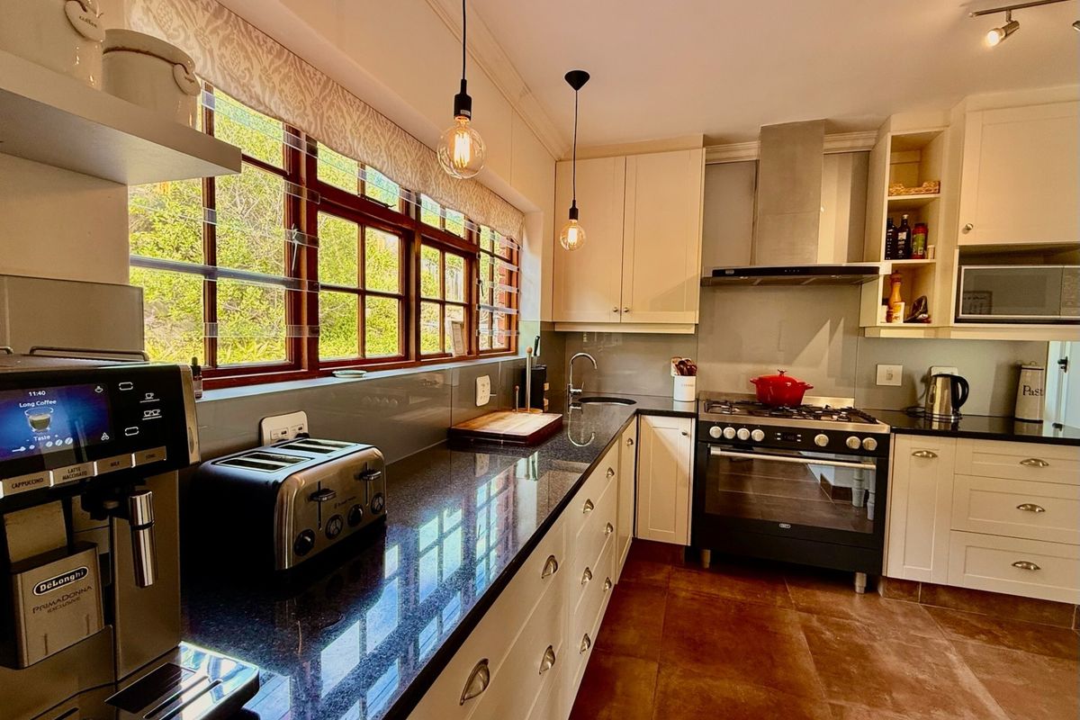 A well-maintained kitchen featuring granite countertops, built-in cabinetry, a gas stove with extractor fan, and large windows providing natural light.