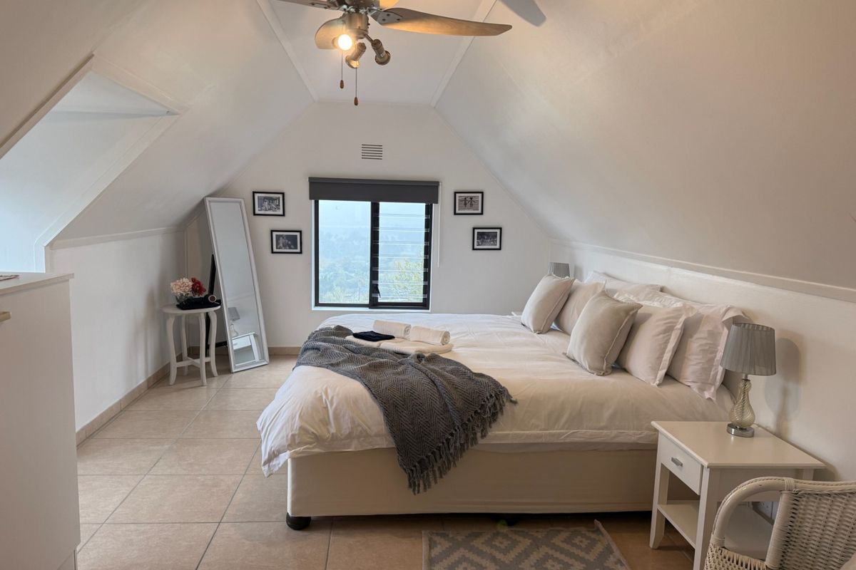 Spacious attic-style bedroom featuring a sloped ceiling, ceiling fan, tiled flooring, and a window with views.