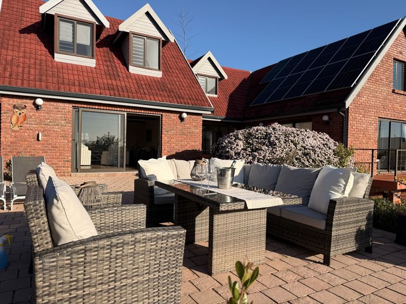 A well-maintained rear exterior view featuring a paved patio area, brick facade, solar panels, and dormer windows under a clear sky.