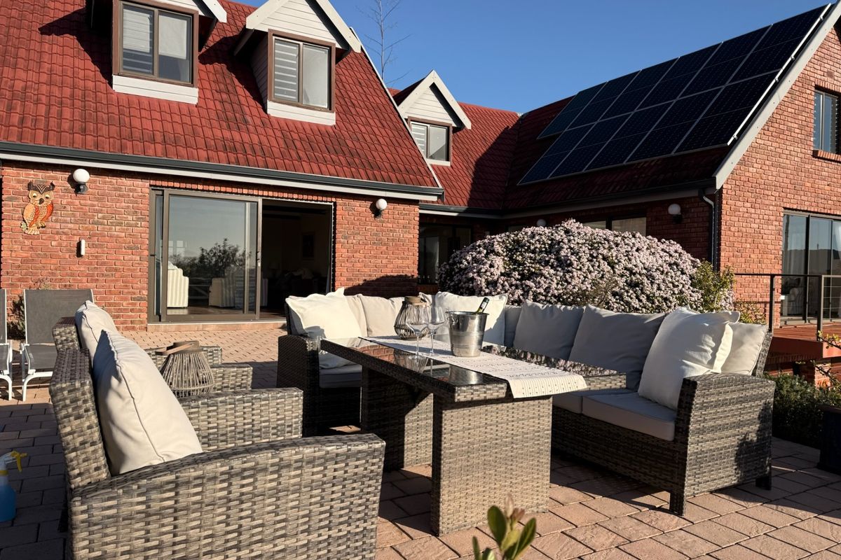 A well-maintained rear exterior view featuring a paved patio area, brick facade, solar panels, and dormer windows under a clear sky.