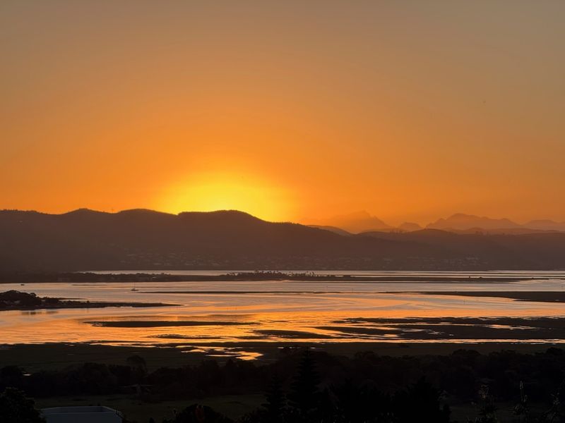 A scenic sunset view overlooking a tranquil estuary and distant mountain range.