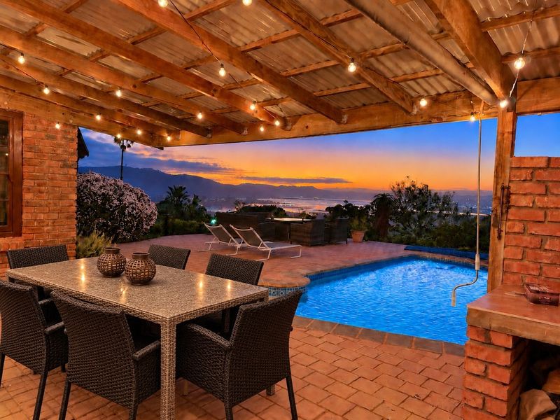 Covered outdoor patio featuring a built-in braai, brick paving, and a swimming pool, overlooking a scenic sunset view.