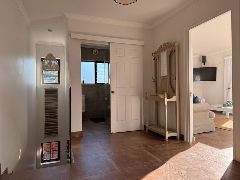 A bright hallway featuring tiled flooring, coving, and access to adjacent rooms, including a bathroom with a sliding door and a staircase.