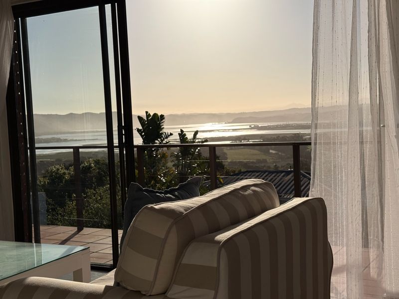 A scenic view of the landscape and water from an interior living space through large sliding glass doors leading to a balcony.