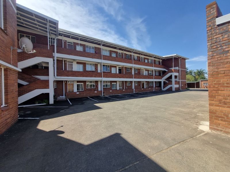Exterior view of a multi-story brick apartment building featuring a paved parking area and external stairwell access.