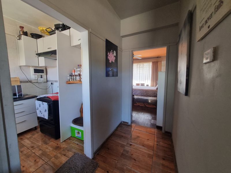 A view from the hallway looking into the kitchen and a bedroom, featuring tiled flooring and functional kitchen cabinetry.