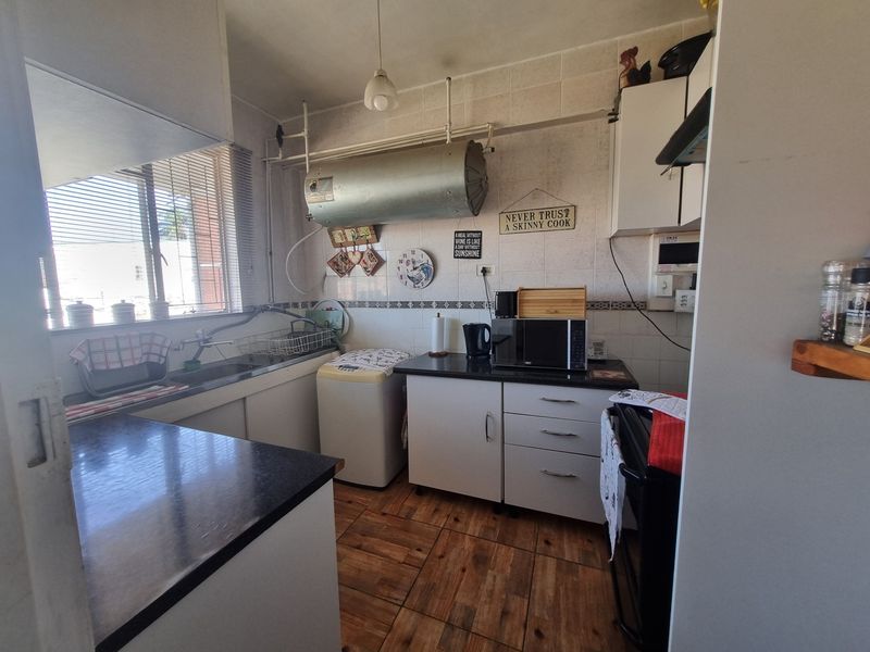 A functional kitchen featuring built-in cabinetry, laminate countertops, and tiled finishes, with an exposed water heater unit and dated aesthetic.
