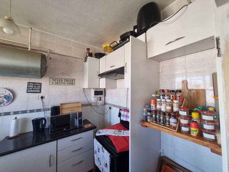 Compact kitchen featuring built-in cabinetry, granite countertops, an extractor fan, and a wall-mounted geyser, offering functional storage and preparation space.