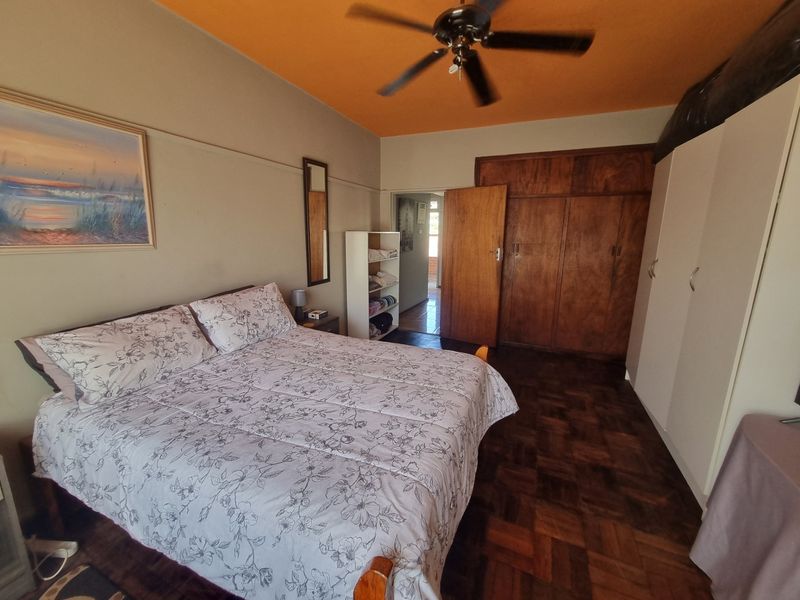 Bedroom featuring parquet flooring, built-in wooden cupboards, additional white wardrobe storage, and a ceiling fan.