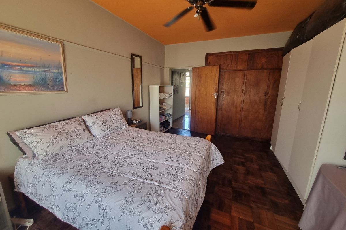 Bedroom featuring parquet flooring, built-in wooden cupboards, additional white wardrobe storage, and a ceiling fan.