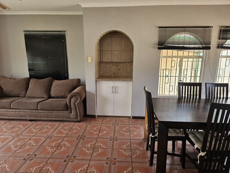 Open plan living and dining area featuring tiled flooring, a built-in arched display niche with granite countertop, and security bars on windows.