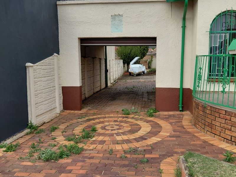 Front exterior view featuring a paved driveway, carport structure, and brick boundary wall with established security features.