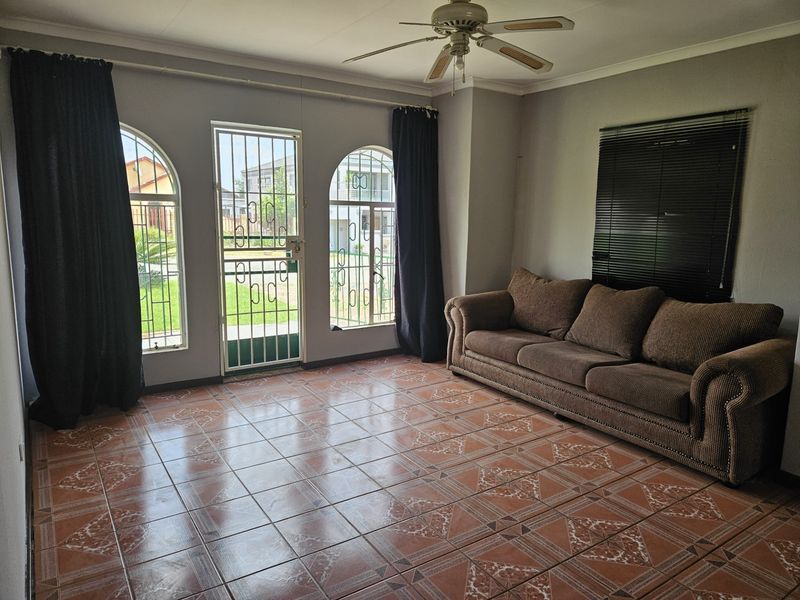 A living room featuring tiled flooring, a ceiling fan, and arched windows with security gates, providing access to the exterior.
