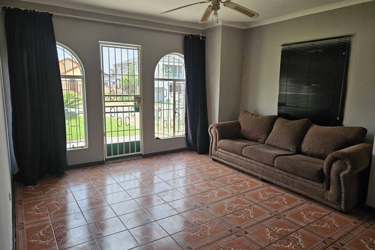 A living room featuring tiled flooring, a ceiling fan, and arched windows with security gates, providing access to the exterior.