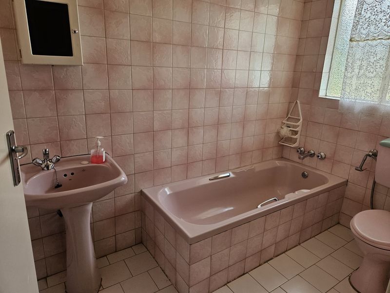 A dated bathroom featuring a pink pedestal basin, matching built-in bathtub, and toilet with full-height wall tiling.