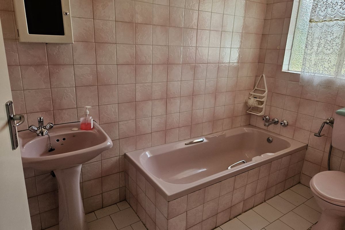 A dated bathroom featuring a pink pedestal basin, matching built-in bathtub, and toilet with full-height wall tiling.