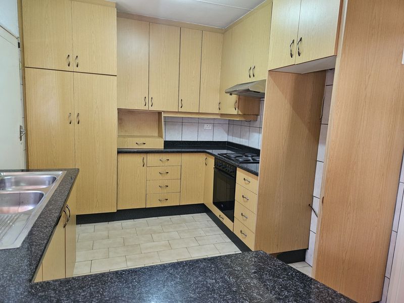 A functional kitchen featuring light wood-finish cabinetry, dark granite countertops, built-in oven and hob, and tiled flooring.