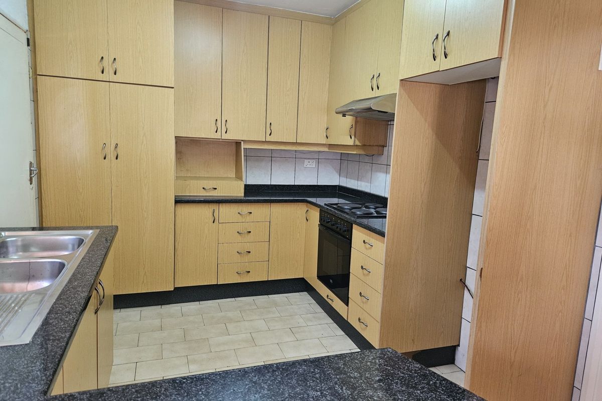 A functional kitchen featuring light wood-finish cabinetry, dark granite countertops, built-in oven and hob, and tiled flooring.