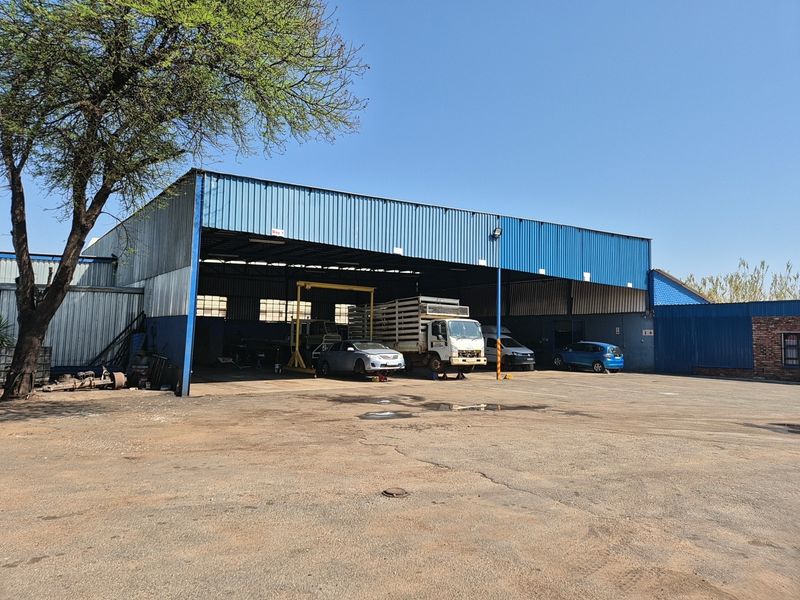 Industrial property featuring a large open-bay workshop with corrugated metal cladding and a spacious paved yard area.