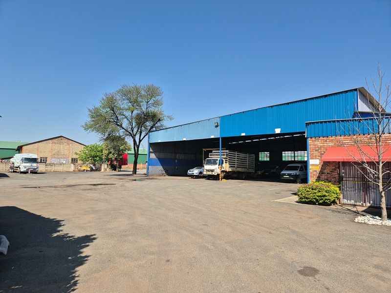 Industrial property featuring a large warehouse structure with metal cladding, a spacious asphalt yard, and a brick facade with an attached awning.