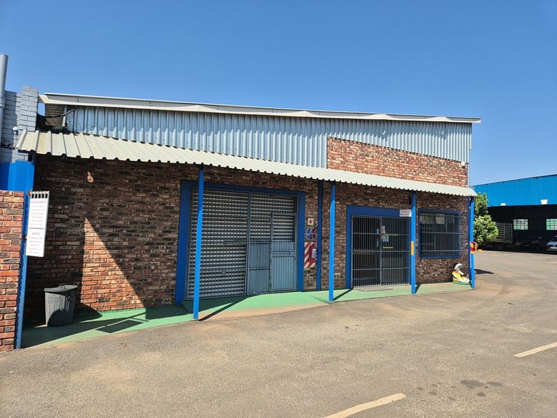 Industrial property exterior featuring a face brick facade, corrugated metal roofing, and secure roller shutter access points with paved driveway frontage.