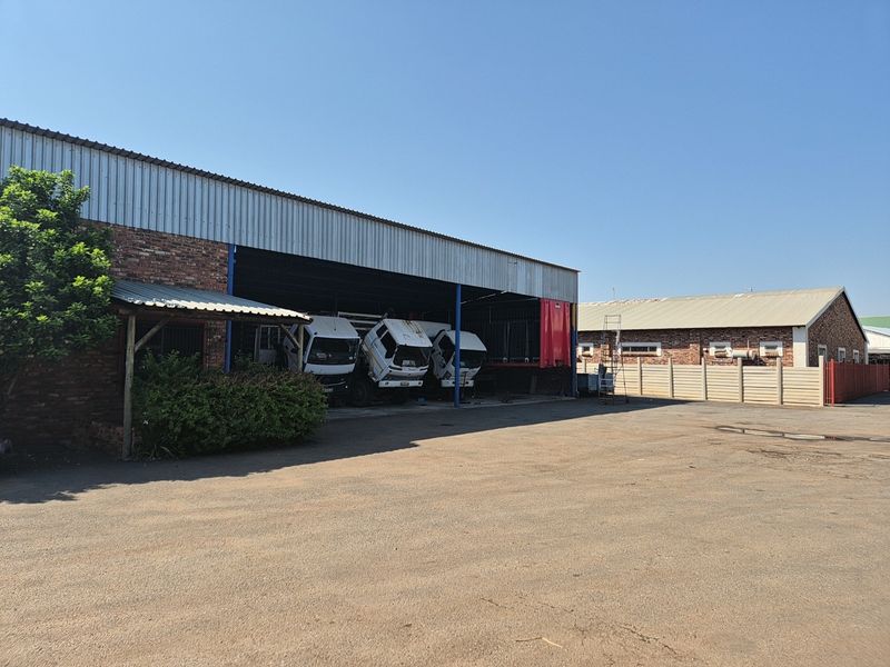 Industrial property featuring an open-sided warehouse bay, exposed brick construction, corrugated metal roofing, and a large paved yard area.