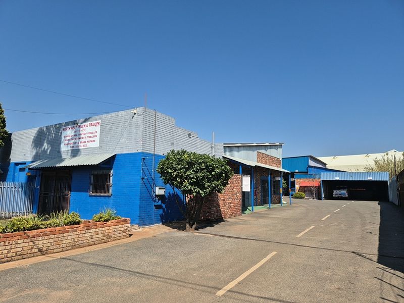 Front exterior view of an industrial property featuring a paved driveway, brick planter, and painted masonry facade with metal roofing.