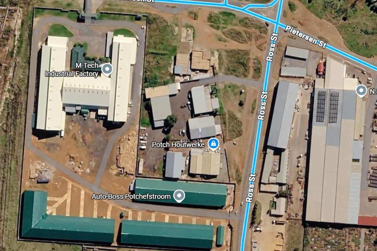 Aerial view of an industrial park featuring multiple factory buildings, warehouses, and paved access roads within a fenced complex.