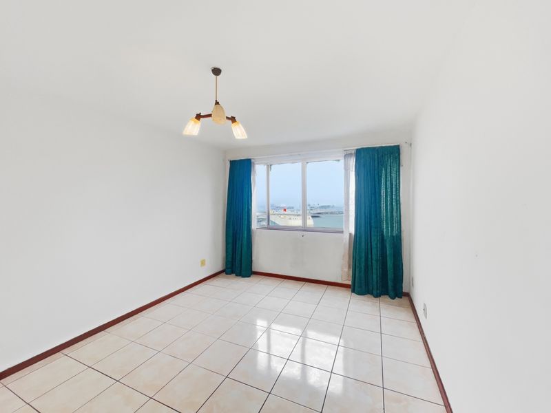 A bright, empty bedroom featuring tiled flooring, neutral walls, and a window with views, providing a blank canvas for personalization.